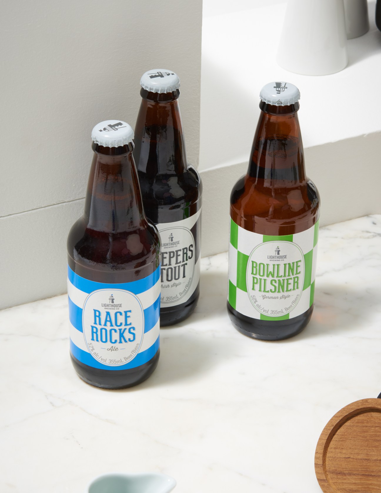 Three beer bottles from Lighthouse Brewing Company displayed on a white surface.