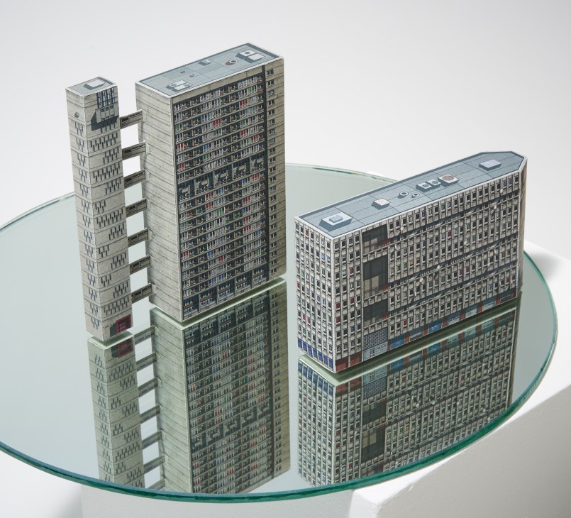 Cardboard architectural models of brutalist London buildings displayed on a curved glass base.