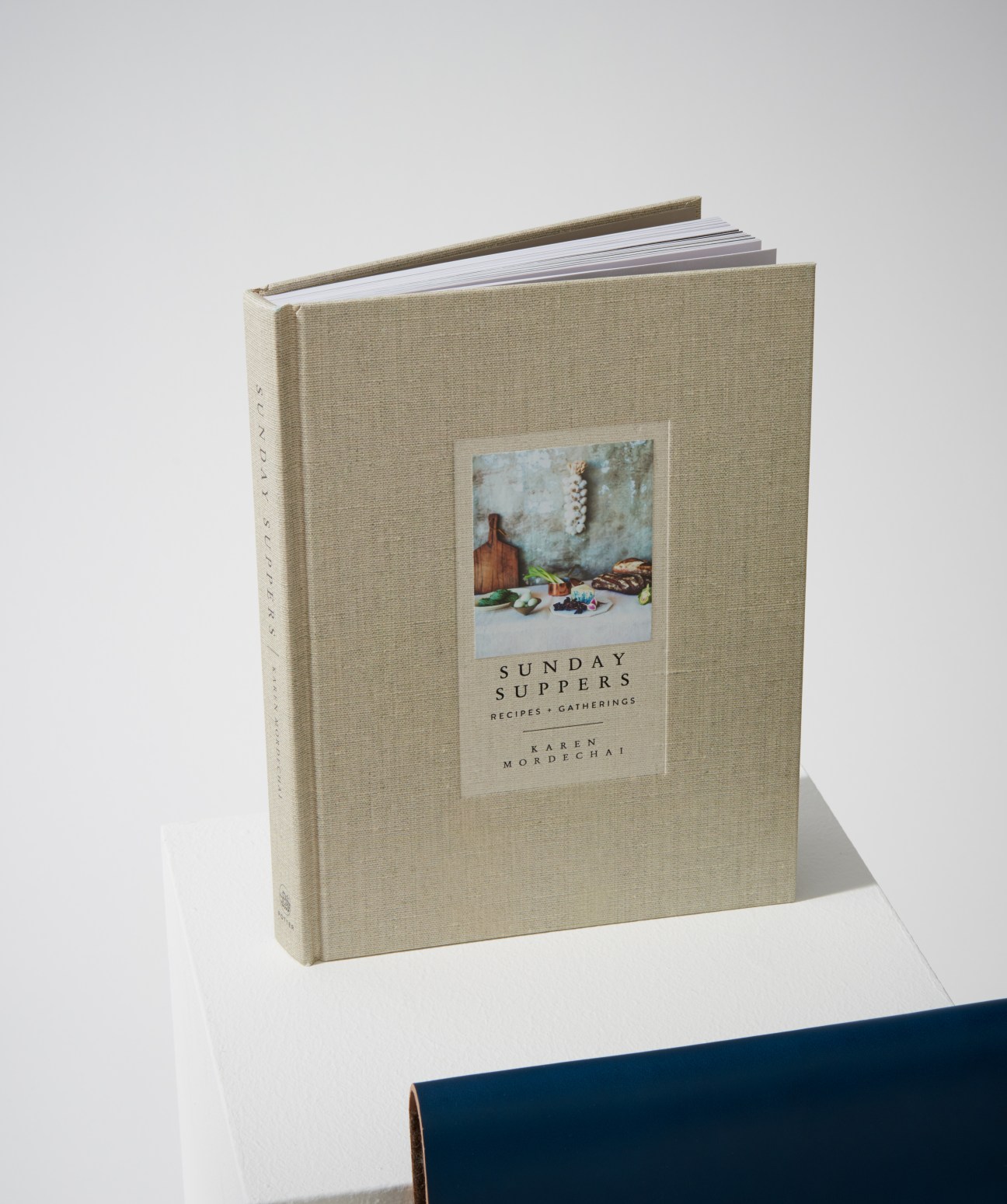 Sunday Suppers cookbook with cream linen cover and embedded photograph of food and kitchen items by Karen Mordechai.
