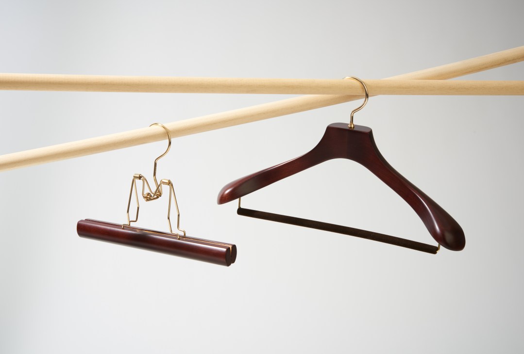 Two wooden hangers with brass hooks hanging from wooden rods against a gray background.