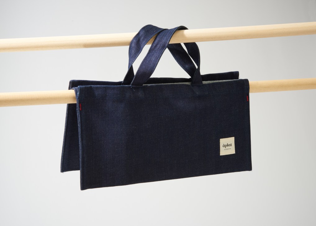 Dark navy organic cotton Àplat tote bag with denim-colored handles hanging on wooden rods.