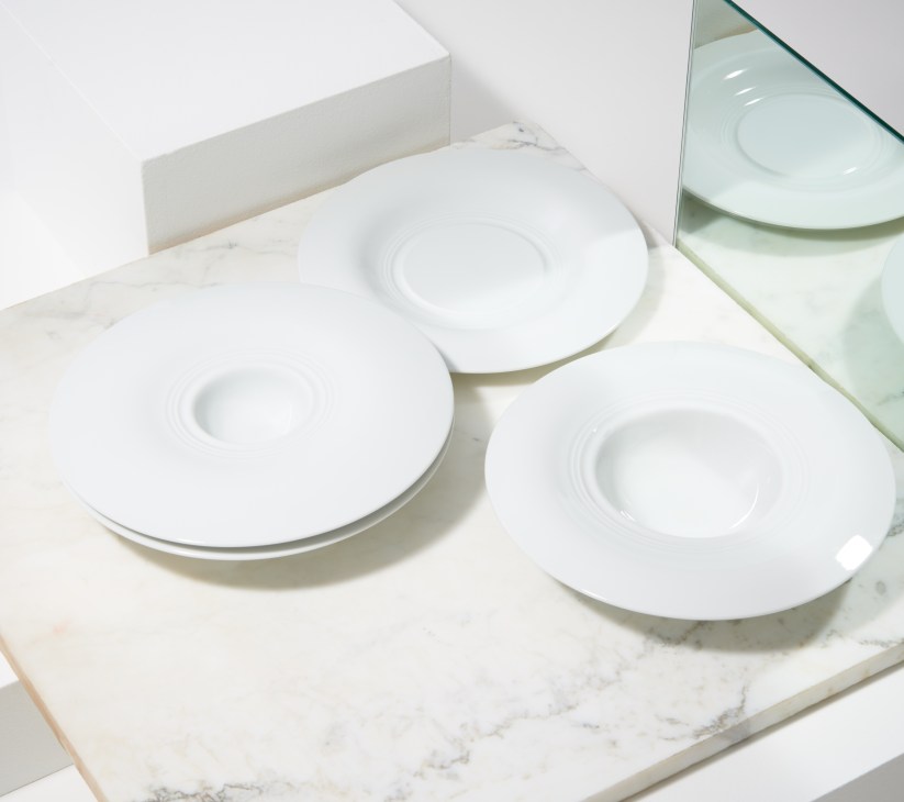 Three white porcelain plates with concentric ring design on marble surface with glass mirror.