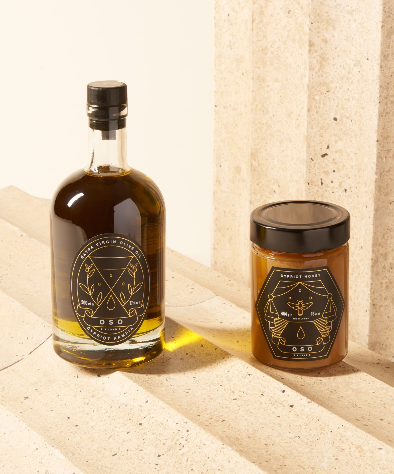 Bottle of PS Lambis extra virgin olive oil and jar of Cypriot honey with gold foil labels on a stone surface.