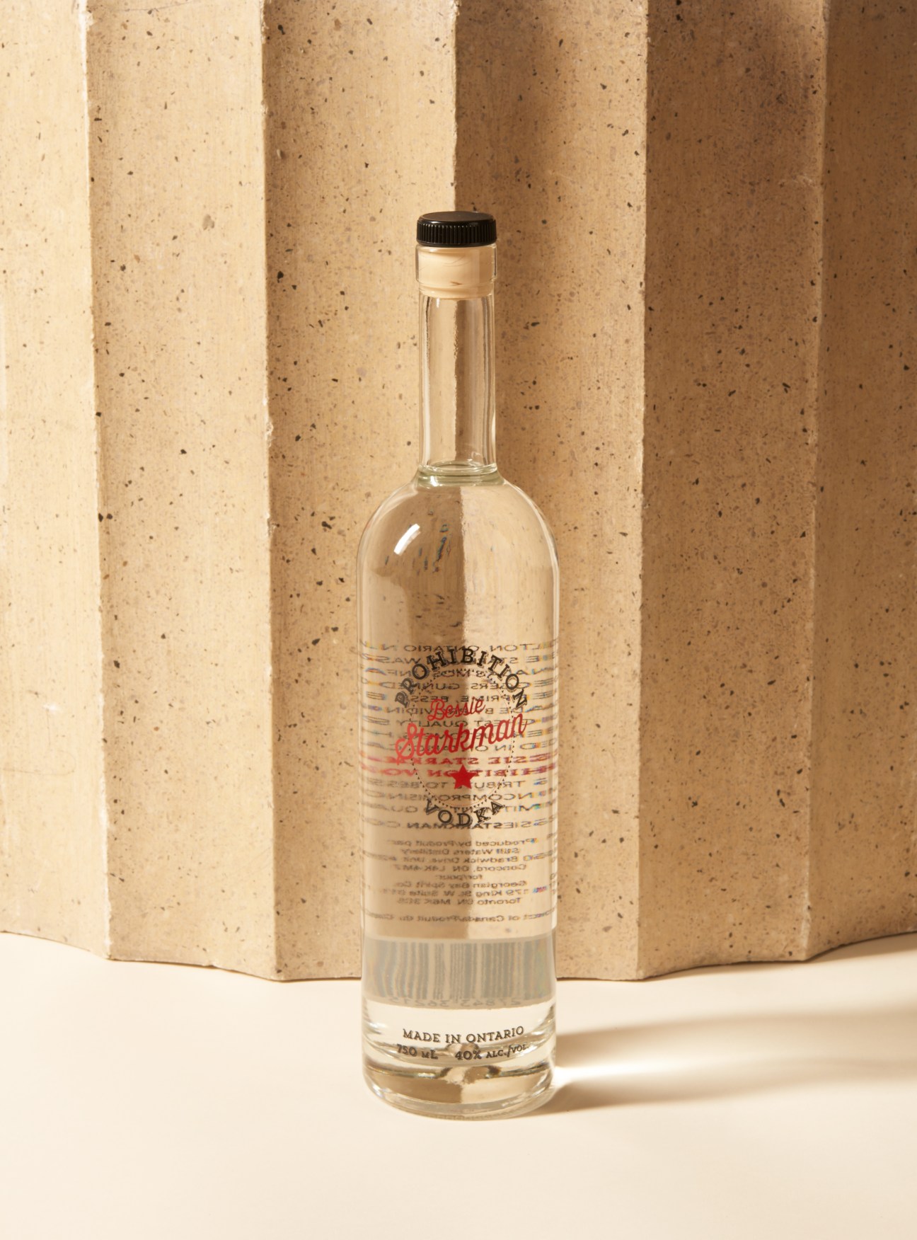 Bottle of Bessie Starkman Prohibition Vodka, Ontario-made, displayed against textured beige background.