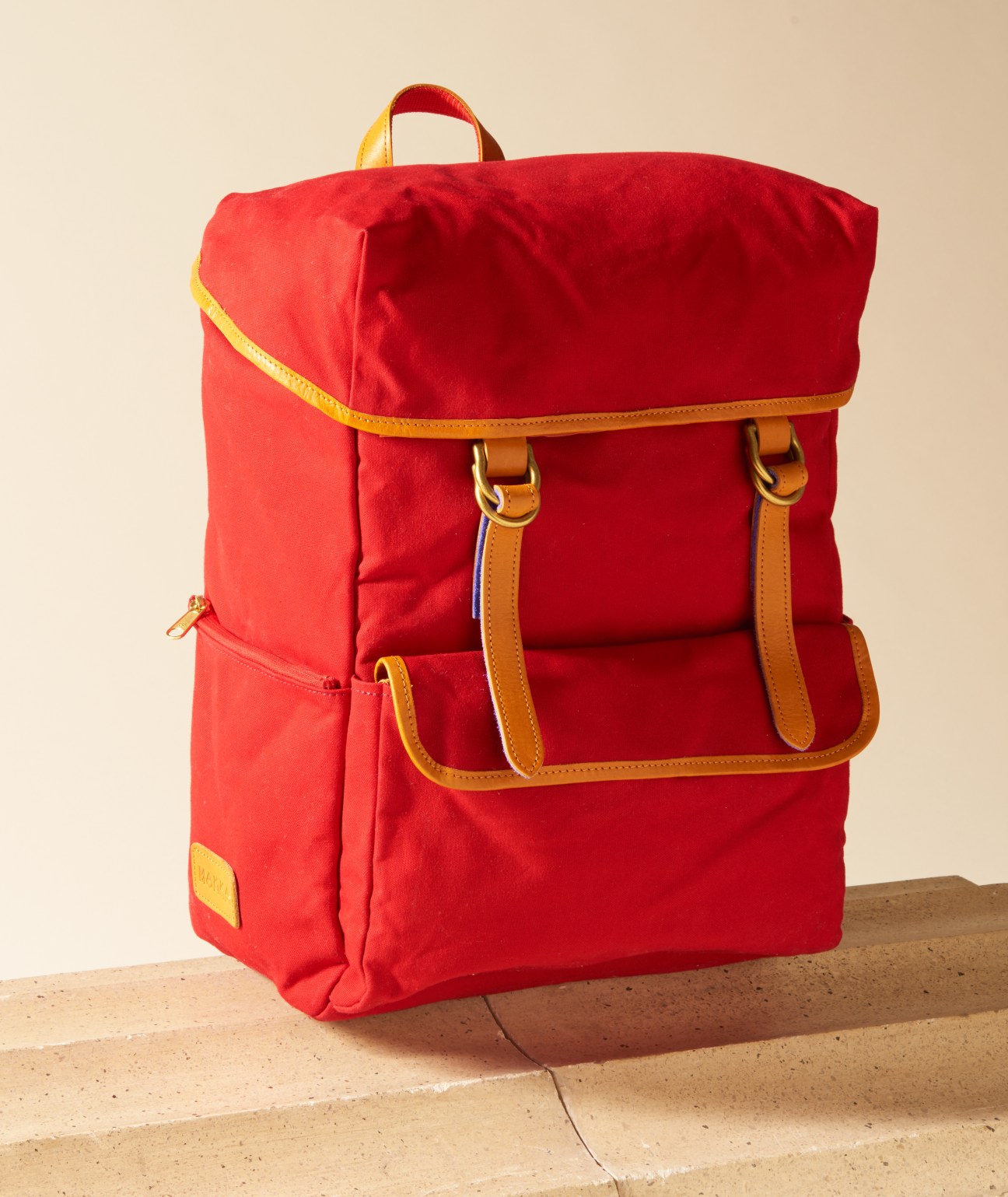 Red canvas backpack with tan leather straps and yellow trim by Makkamon.