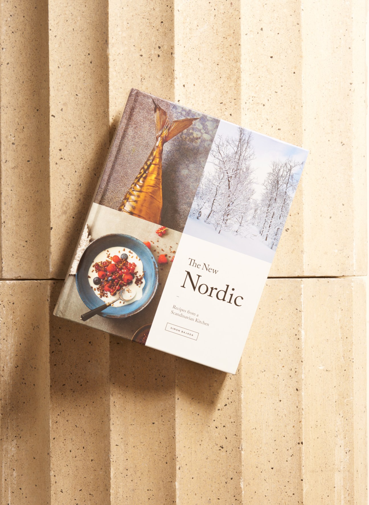 The New Nordic cookbook by Simon Bajada displayed on a cork surface with Nordic-inspired imagery.