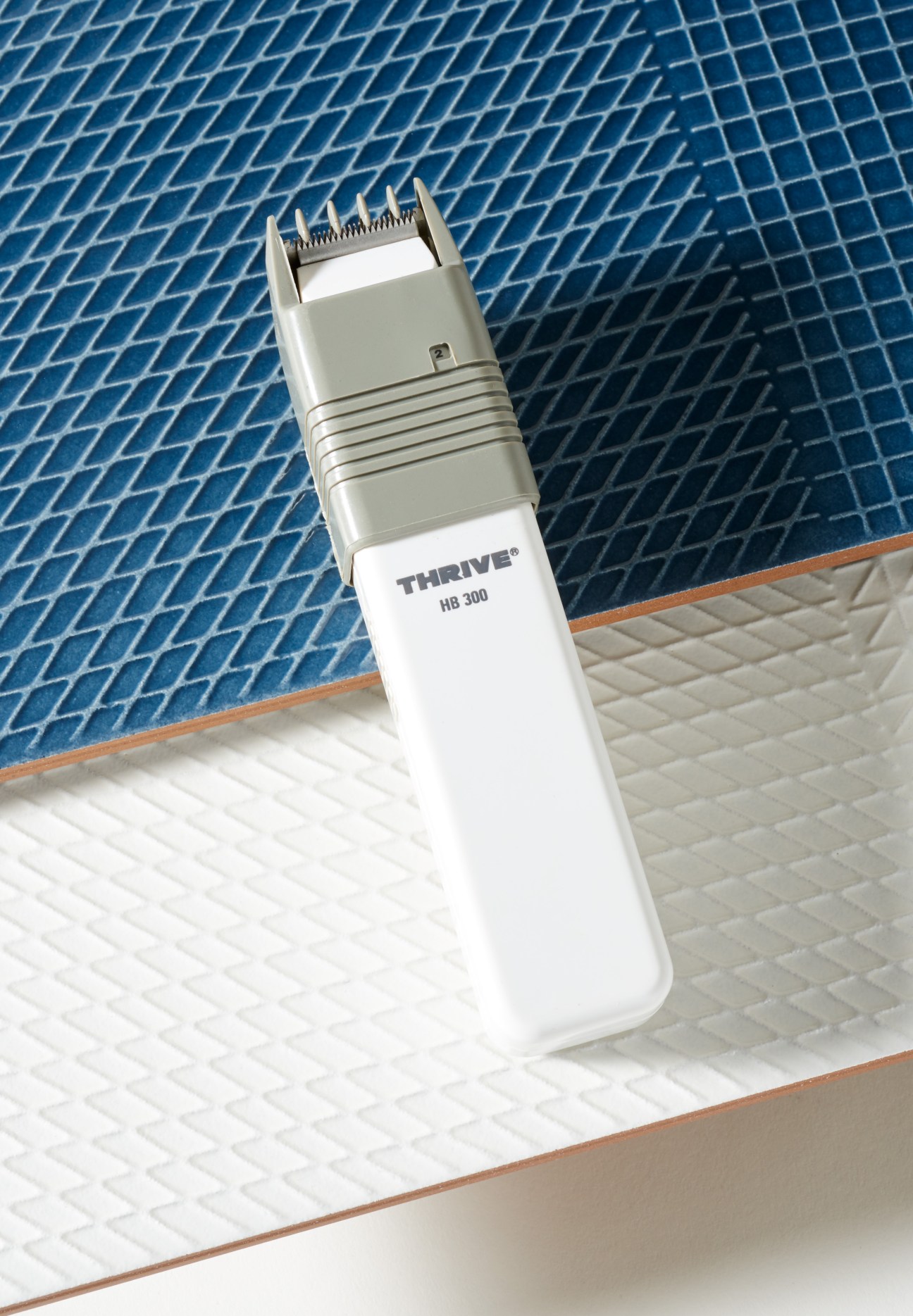 White Daito-Thrive HB 300 cordless hair clipper displayed on blue and white tiled background.