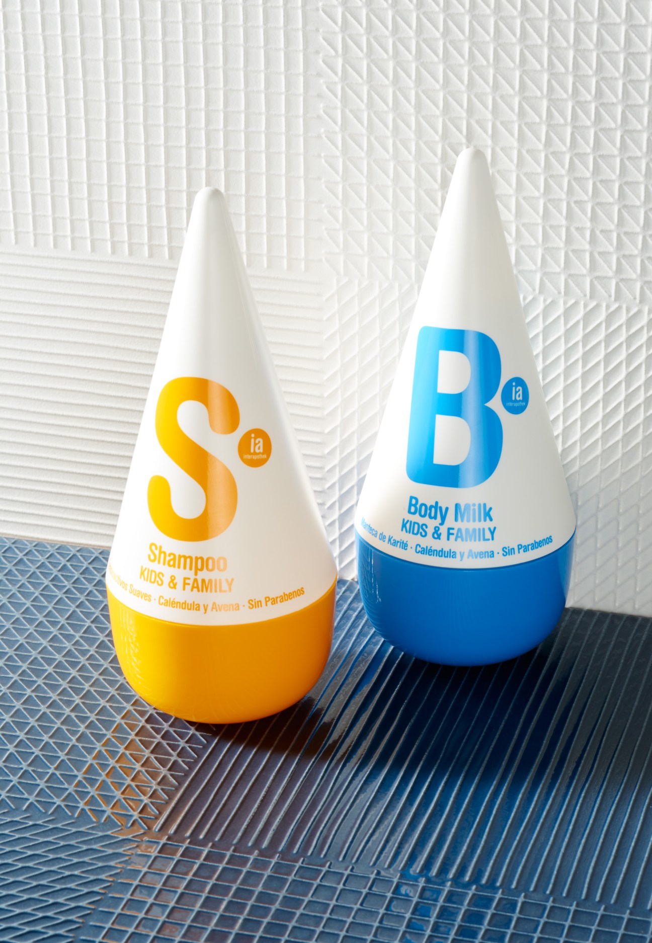 Two cone-shaped bottles of Interapothek baby products in yellow shampoo and blue body milk with textured tile background.