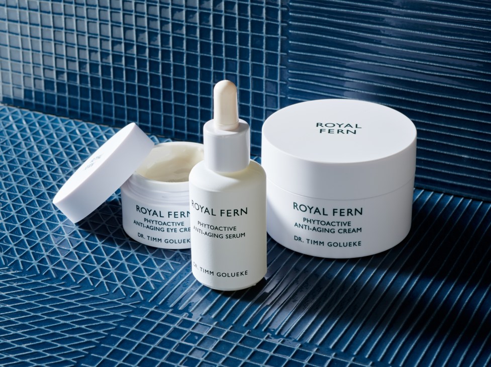 Royal Fern phytoactive anti-aging skincare products including eye cream, serum, and face cream by Dr. Timm Golueke displayed on blue textured tile background.
