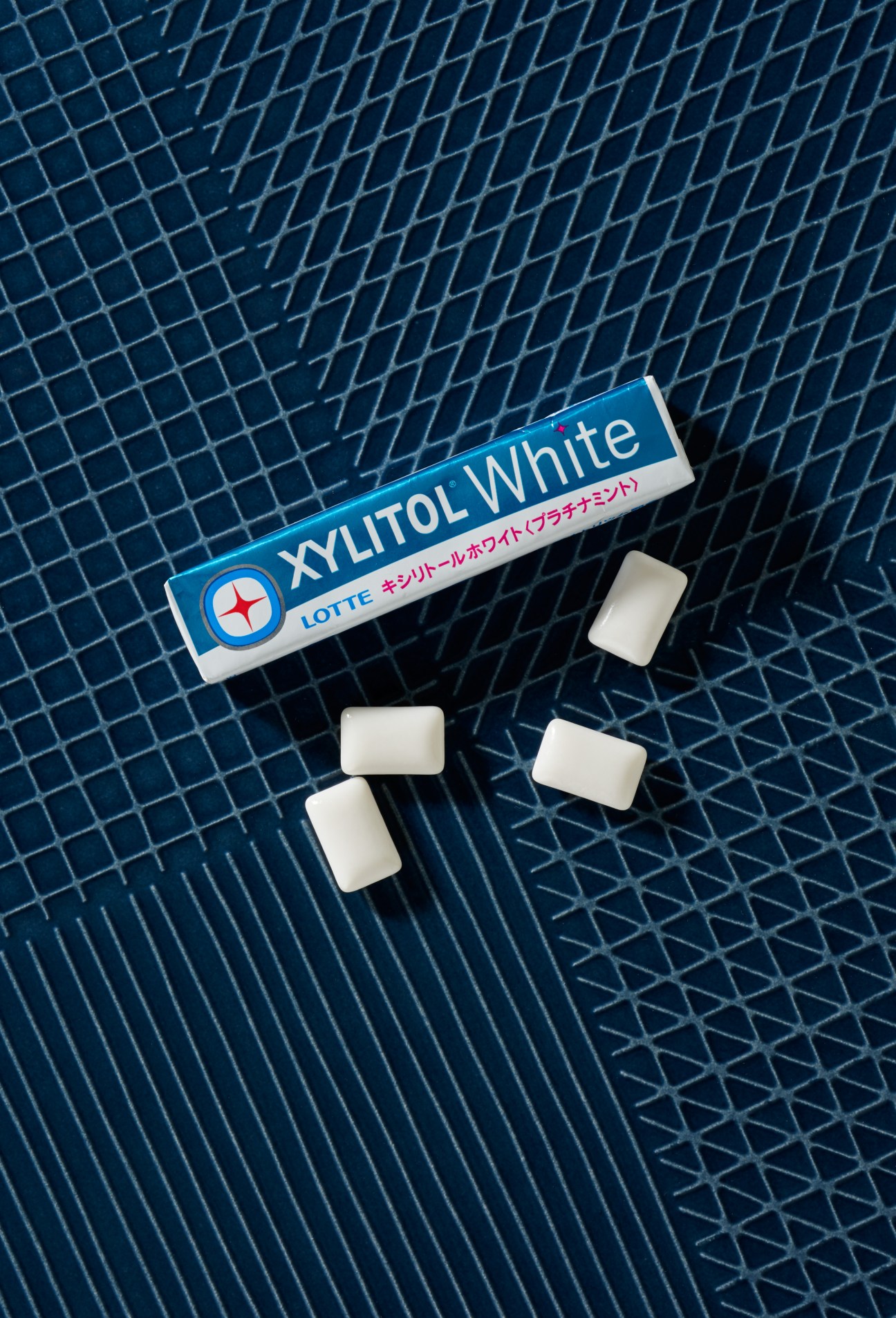 Lotte Full Swing Xylitol White chewing gum pack with individual white pieces on blue tiled background.