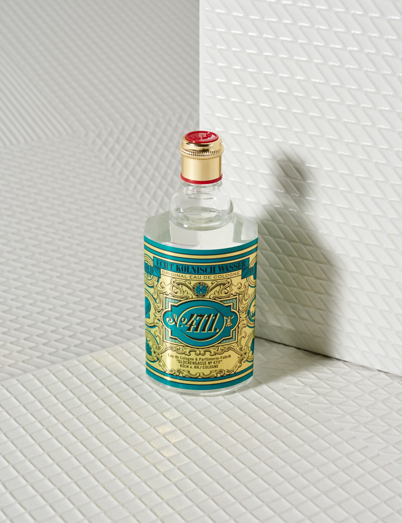 A bottle of 4711 Original Eau de Cologne with a turquoise and gold label and red cap on white tiled background.