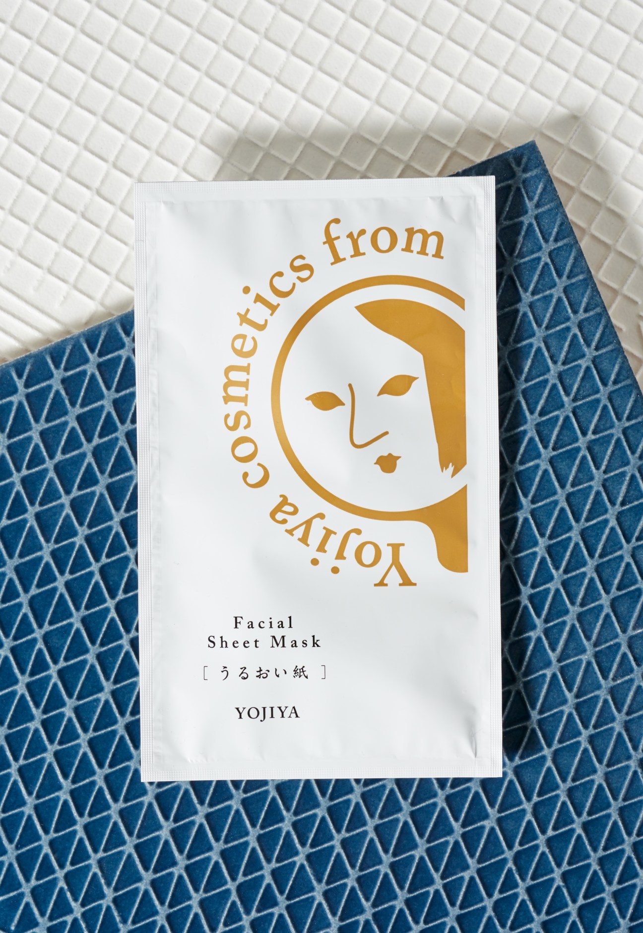 Yojiya facial sheet mask package with gold illustration of woman's face on white background.