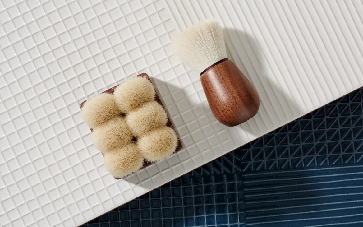 Face and body brushes with soft goat-hair bristles and dark walnut handles by Suvé displayed on white tile.