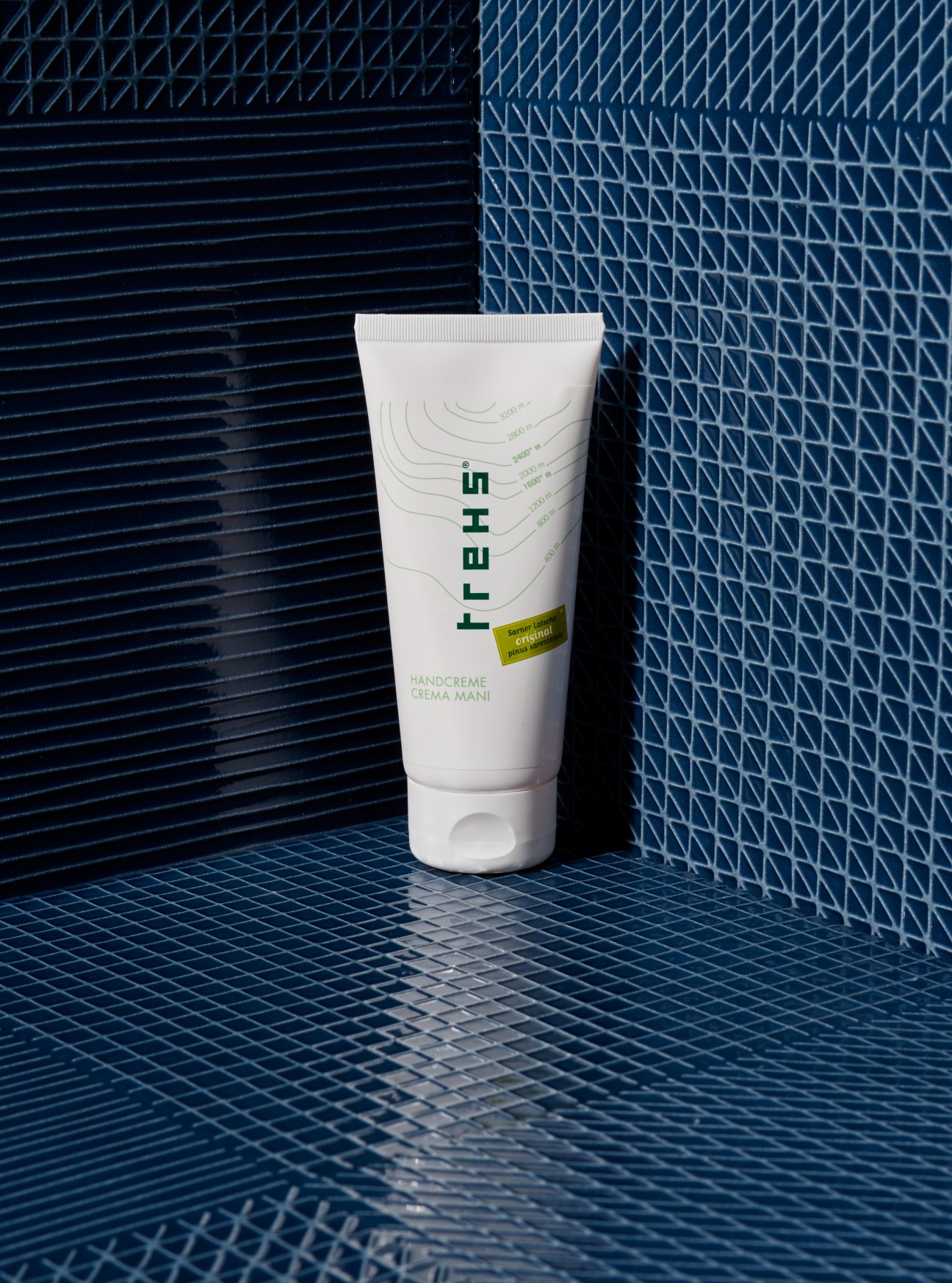 Trehs hand cream tube displayed on blue textured tile background.