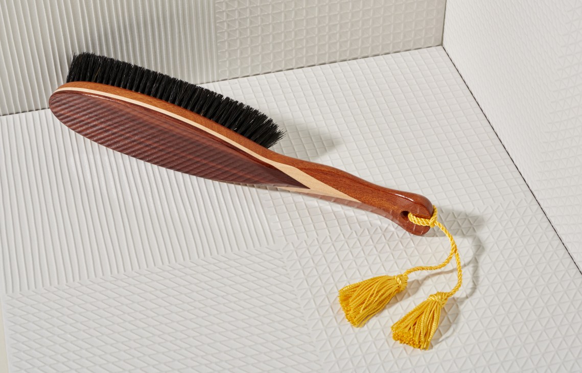 Wooden-handled clothes brush with black bristles and yellow tassel on white textured background.