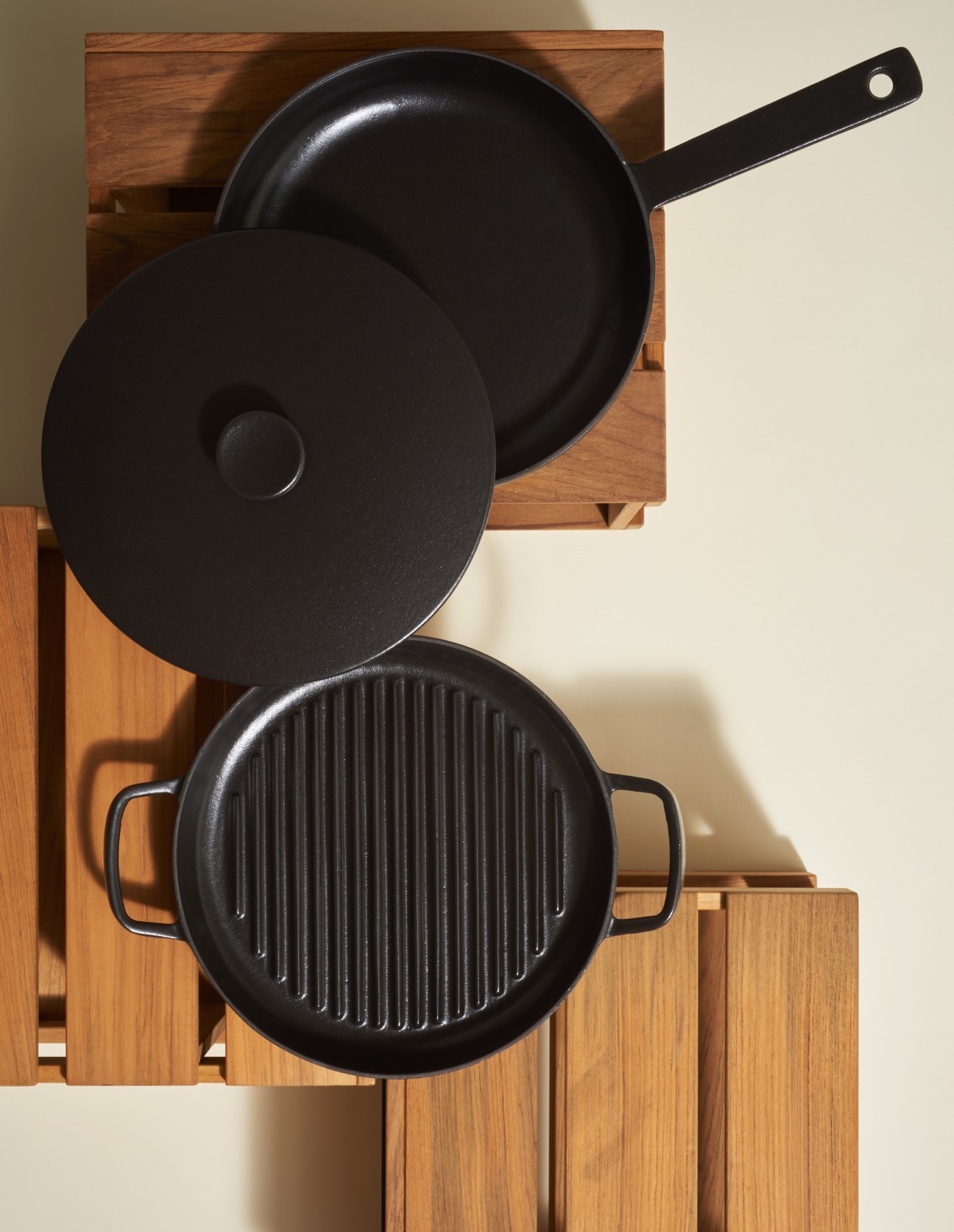 Three black cast-iron pans with matt-black enamel finish arranged on wooden boards