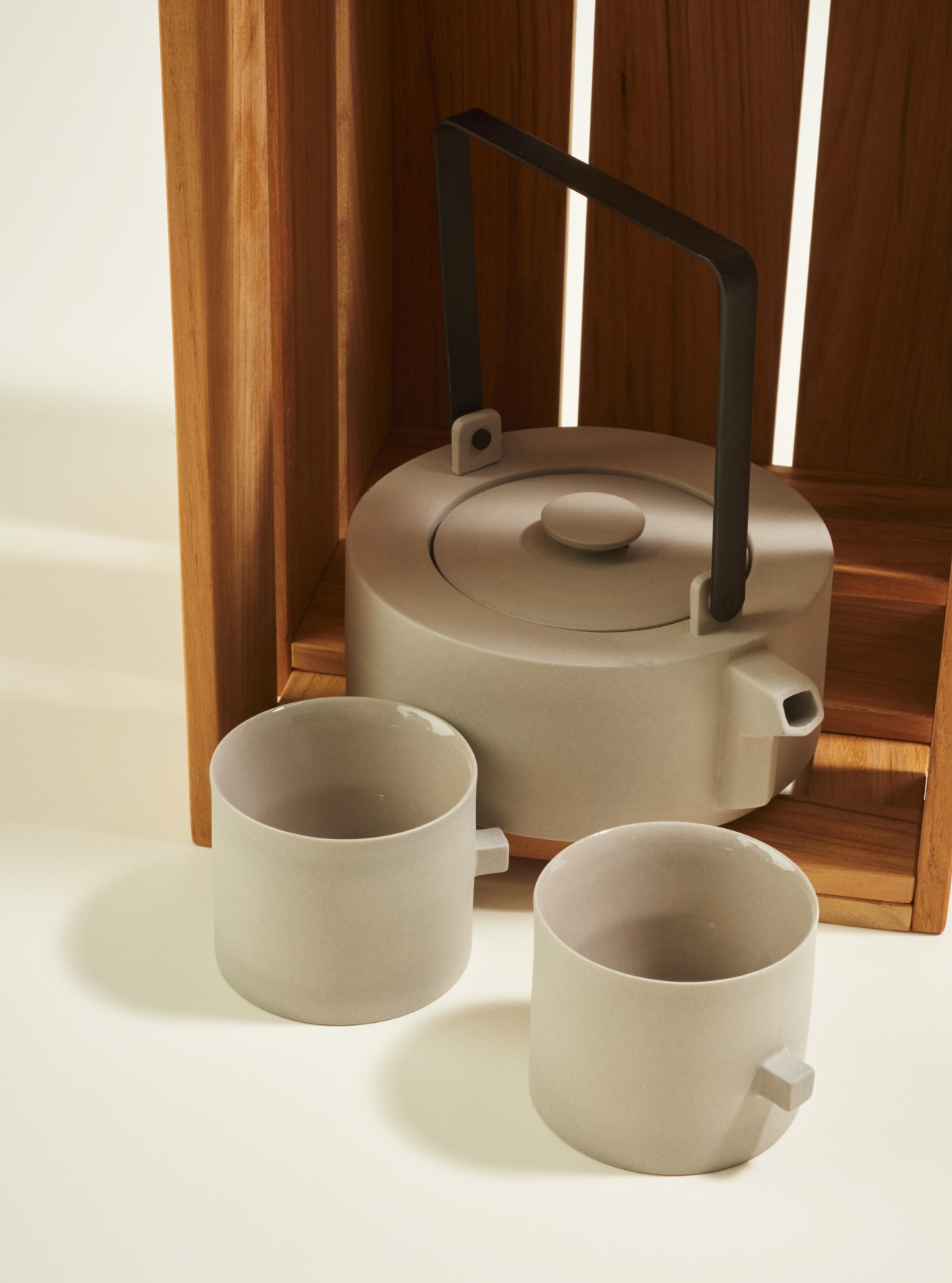 Light grey porcelain teapot with black handle and two matching cups with small squared handles by Round Square Teaware.