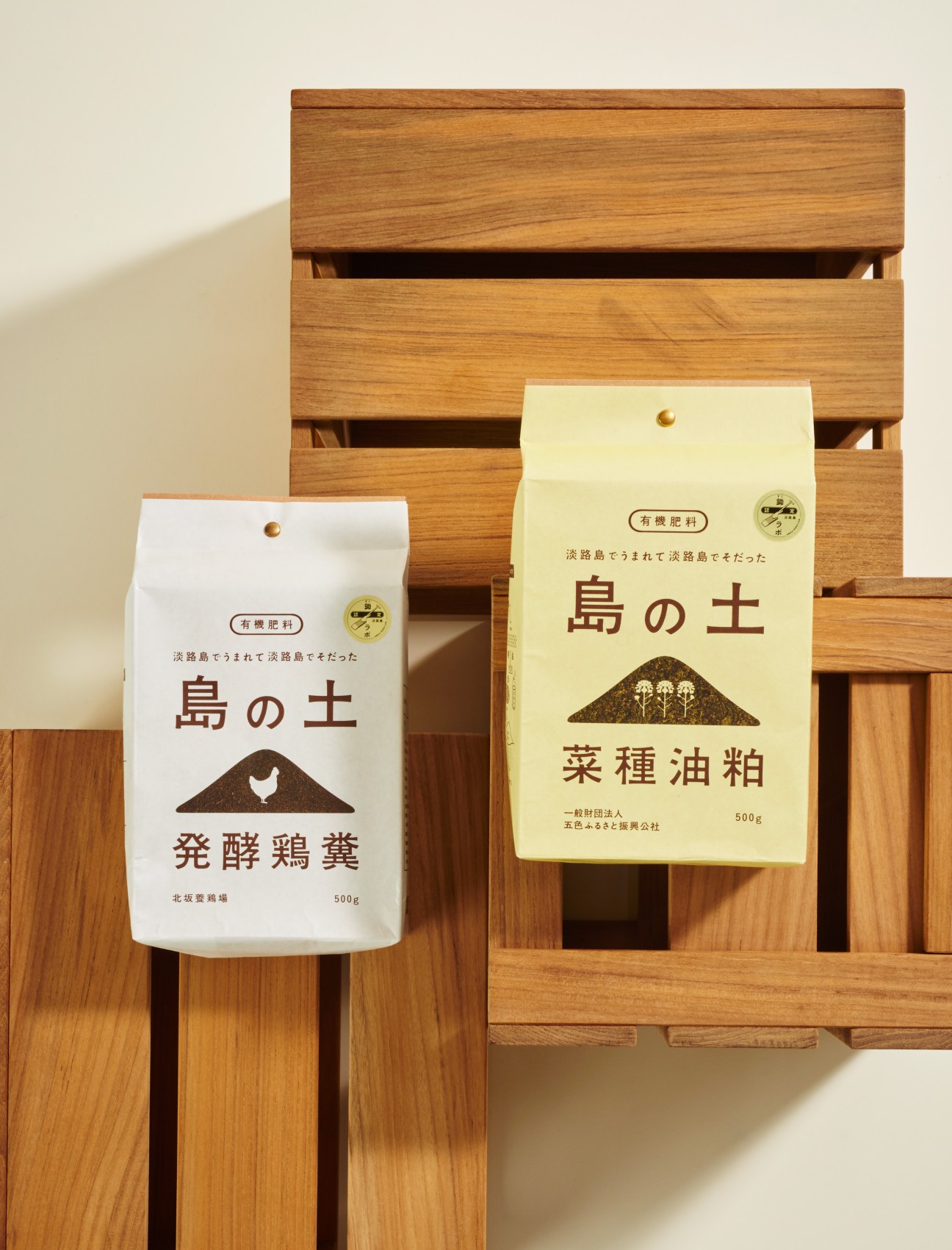 Two packets of Umamu fertiliser with Japanese text displayed against a wooden drawer unit.