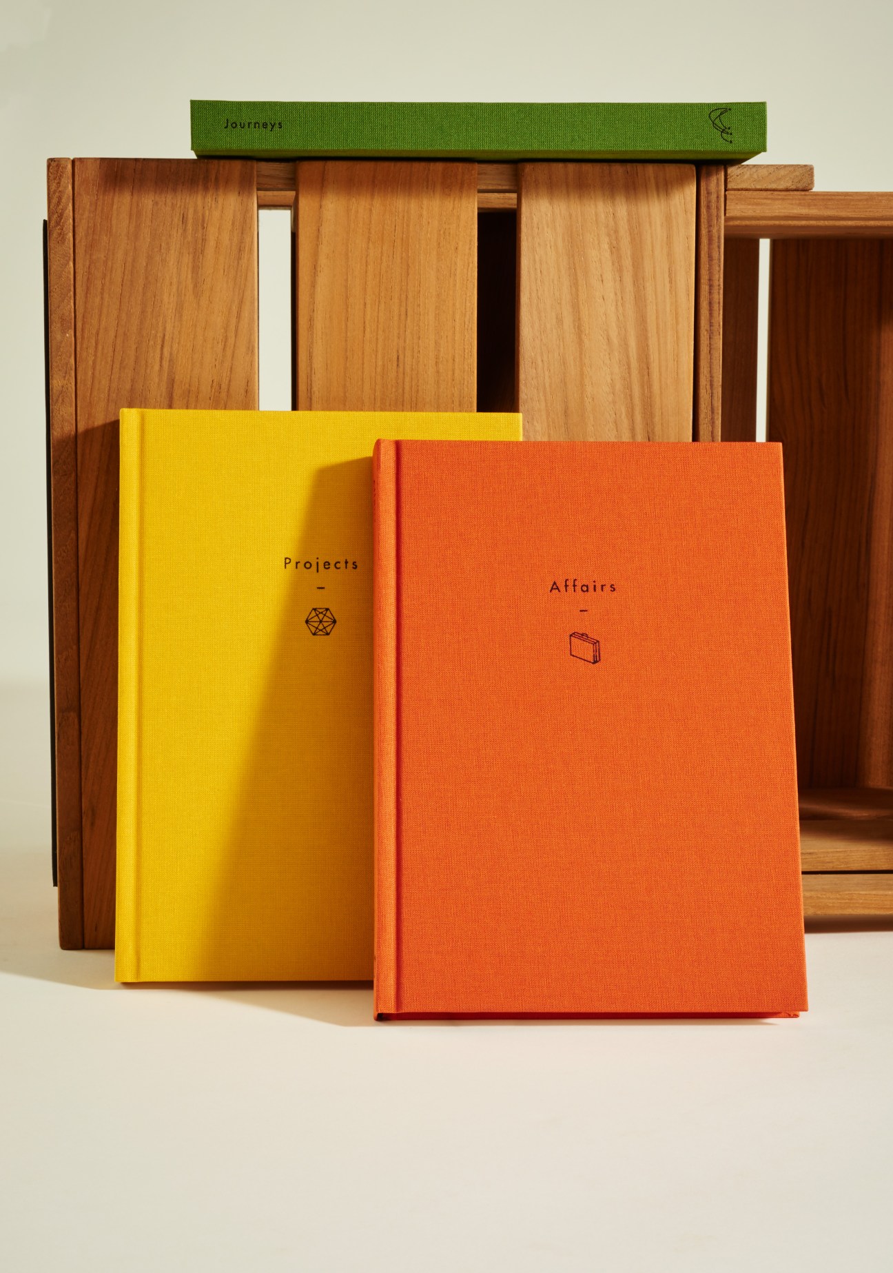 Colorful linen-bound notebooks by The School of Life stacked in front of wooden shelving.