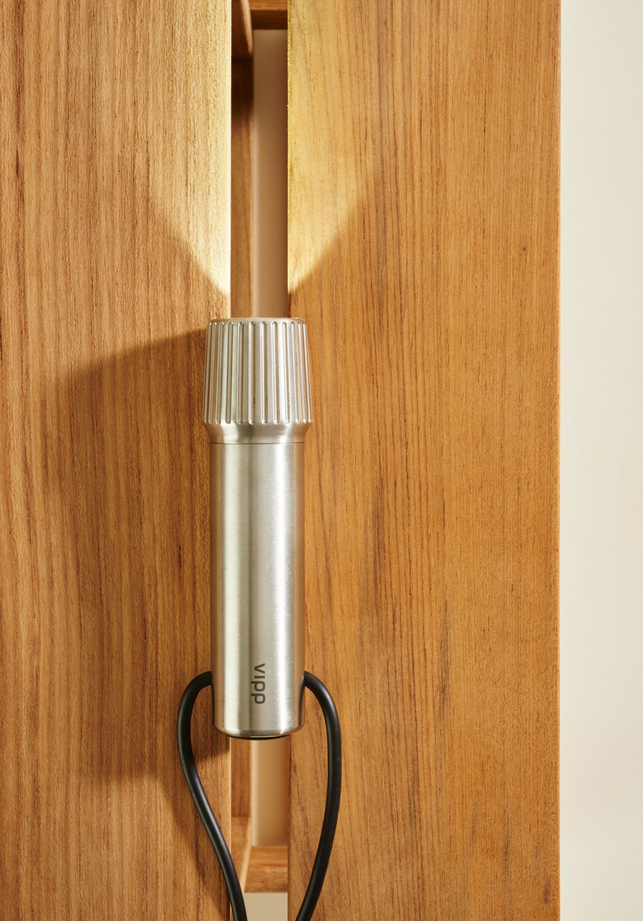 Vipp stainless steel torch with ribbed top grip and black handle against wooden background.