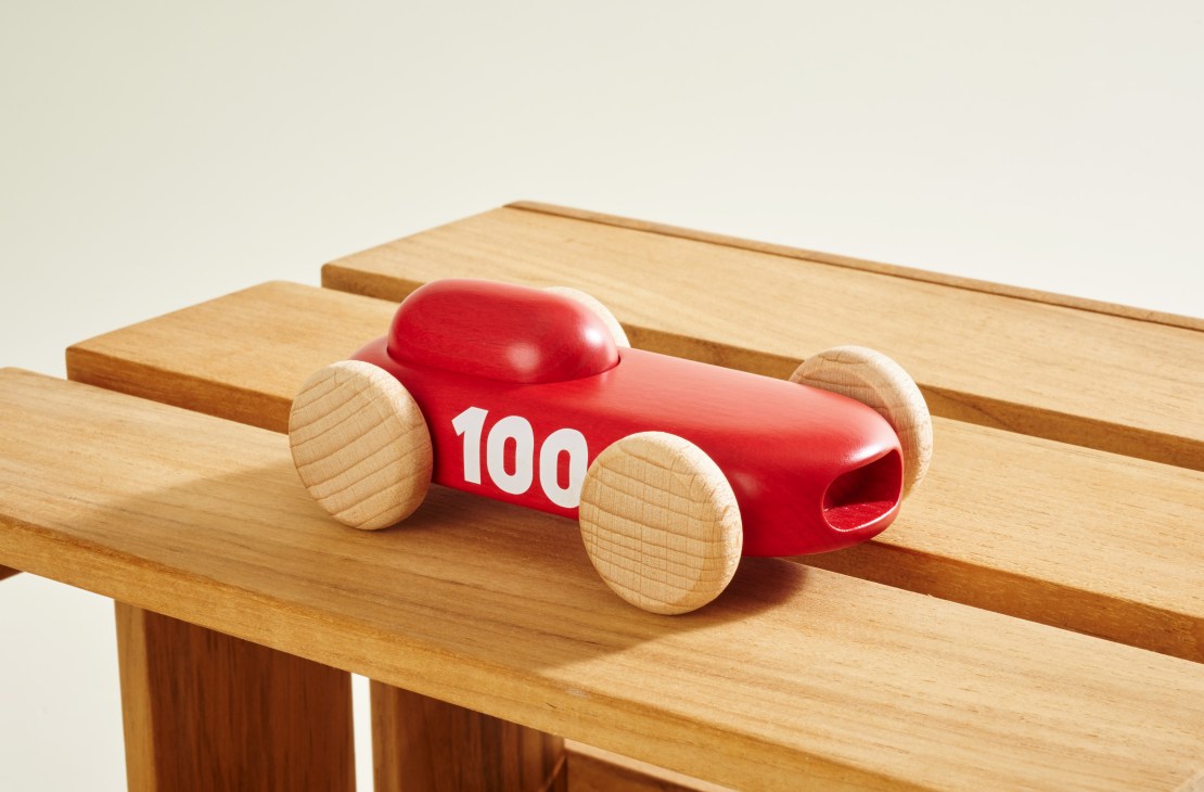 Red wooden toy racing car with white number 100 and natural wood wheels on a wooden table.