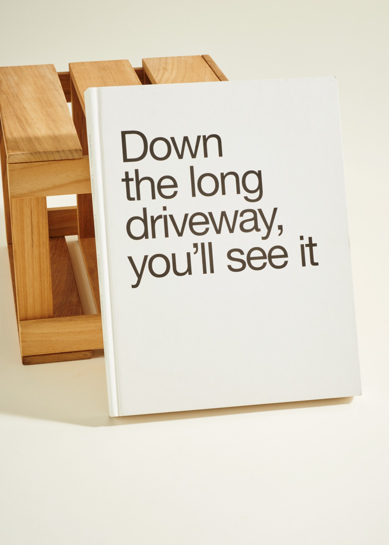 White hardcover book with wooden stand displaying title 'Down the long driveway, you'll see it'