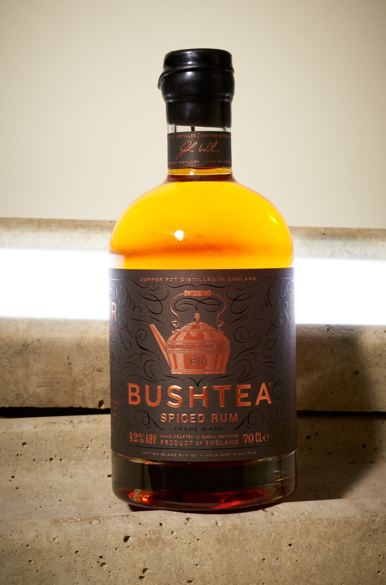 Bushtea Spiced Rum bottle with black label and golden liquid against a neutral background.