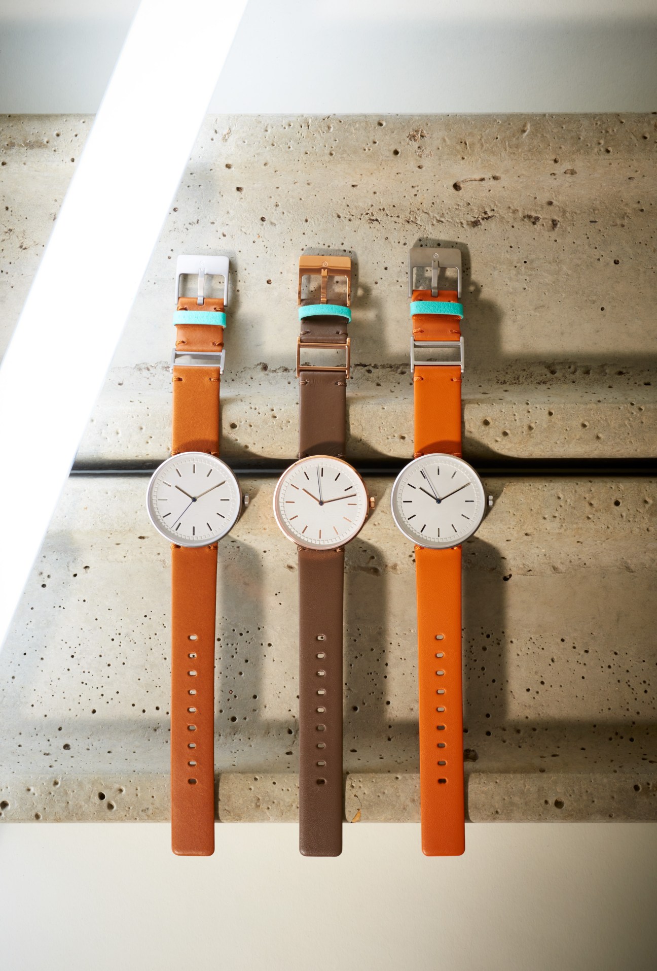 Three Fromhence watches with interchangeable orange and brown leather straps displayed on concrete surface.