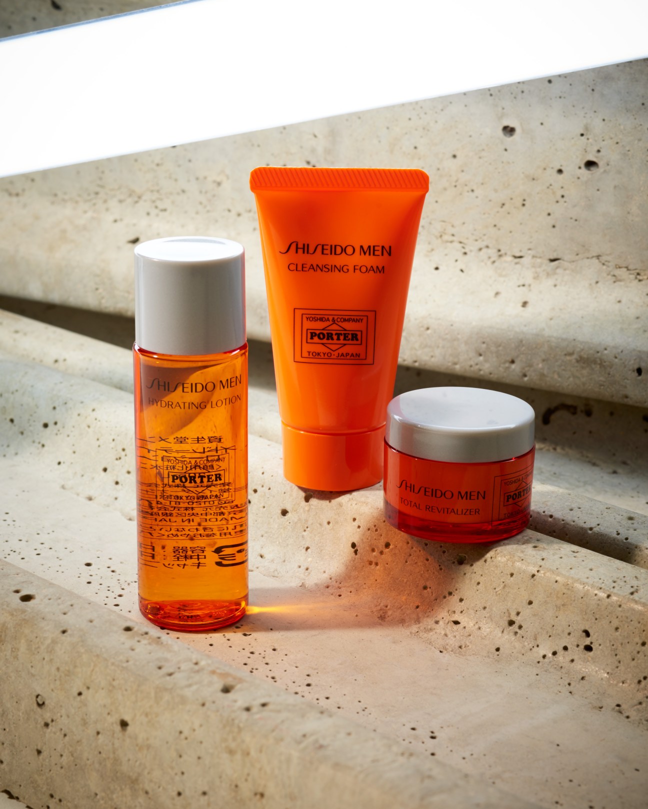 Porter X Shiseido Men skincare kit with orange cleansing foam, hydrating lotion and red revitalizer on concrete surface.