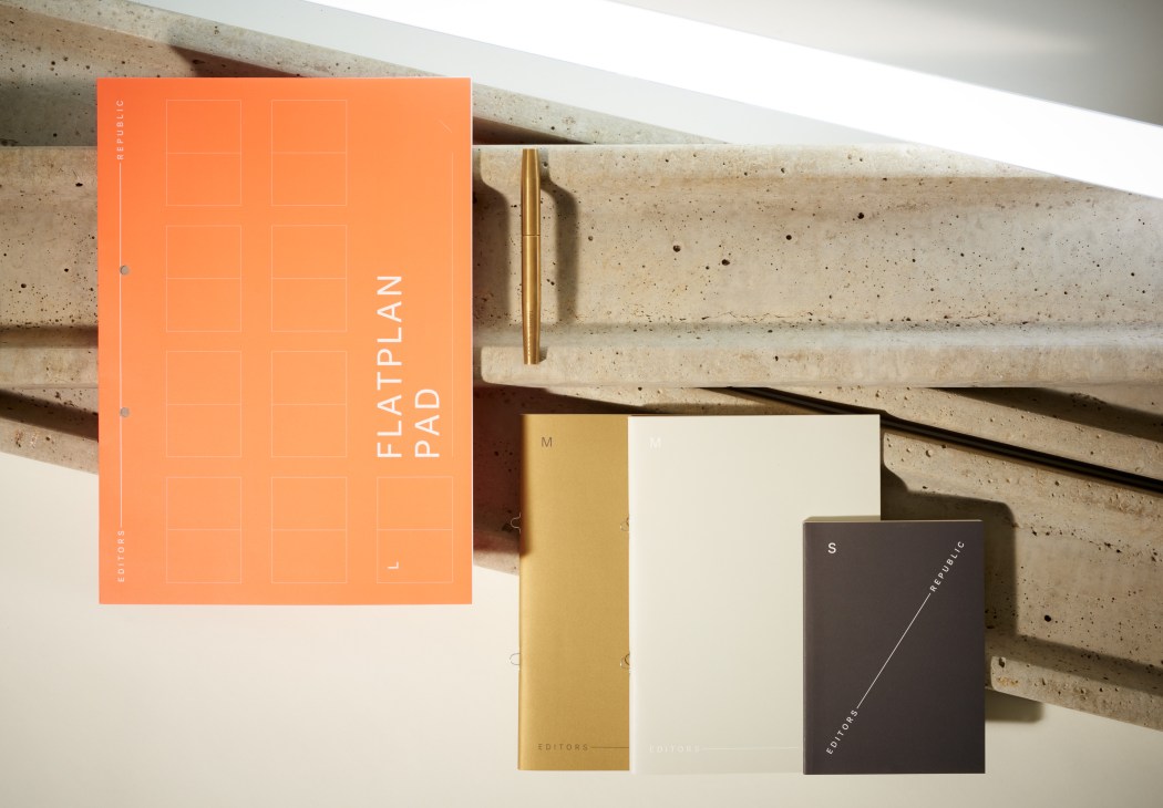 An orange flatplan pad and dark notebooks displayed against concrete shelving.