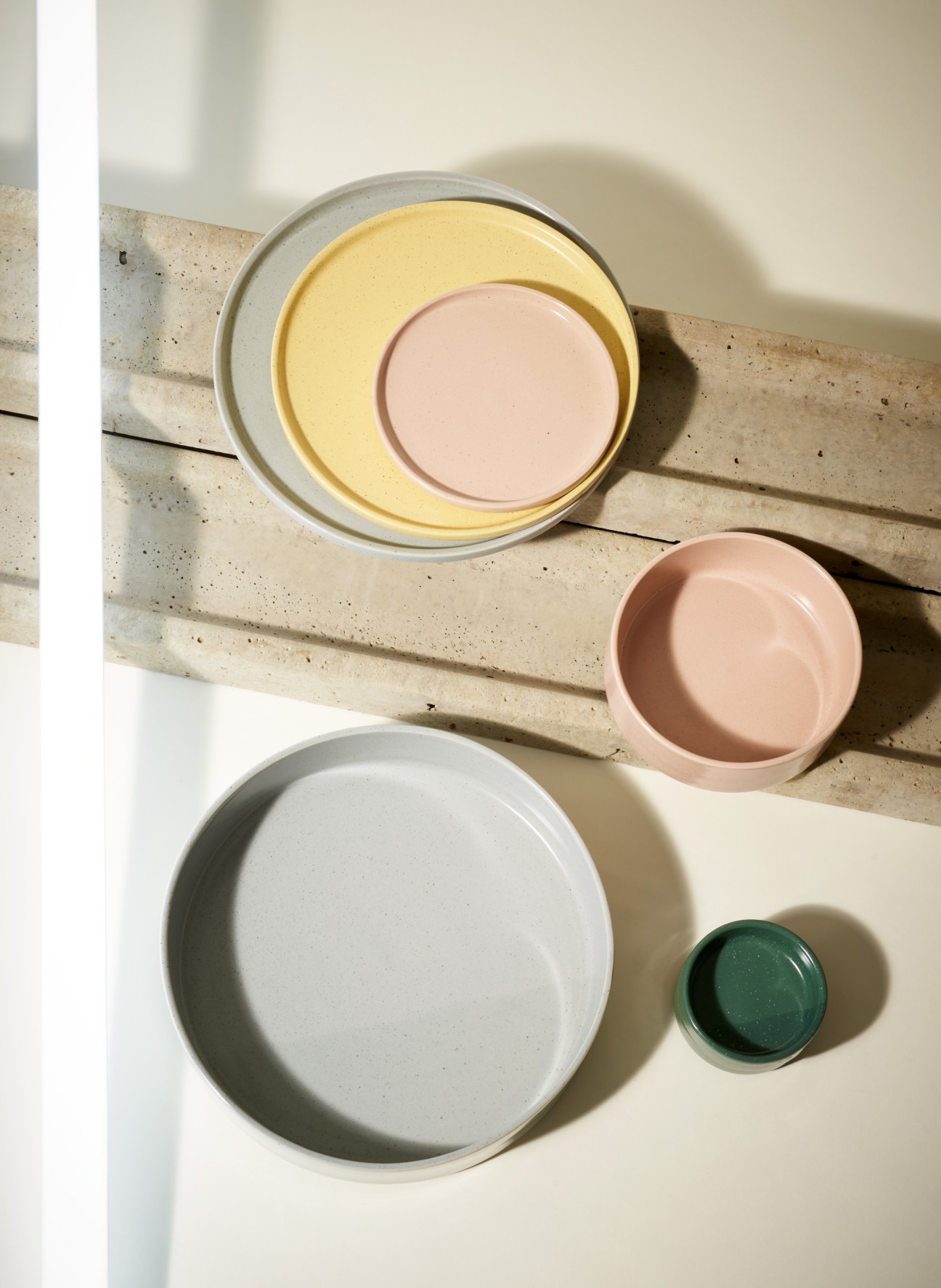 Colorful ceramic bowls and cups in yellow, pink, white and green arranged on a concrete surface.