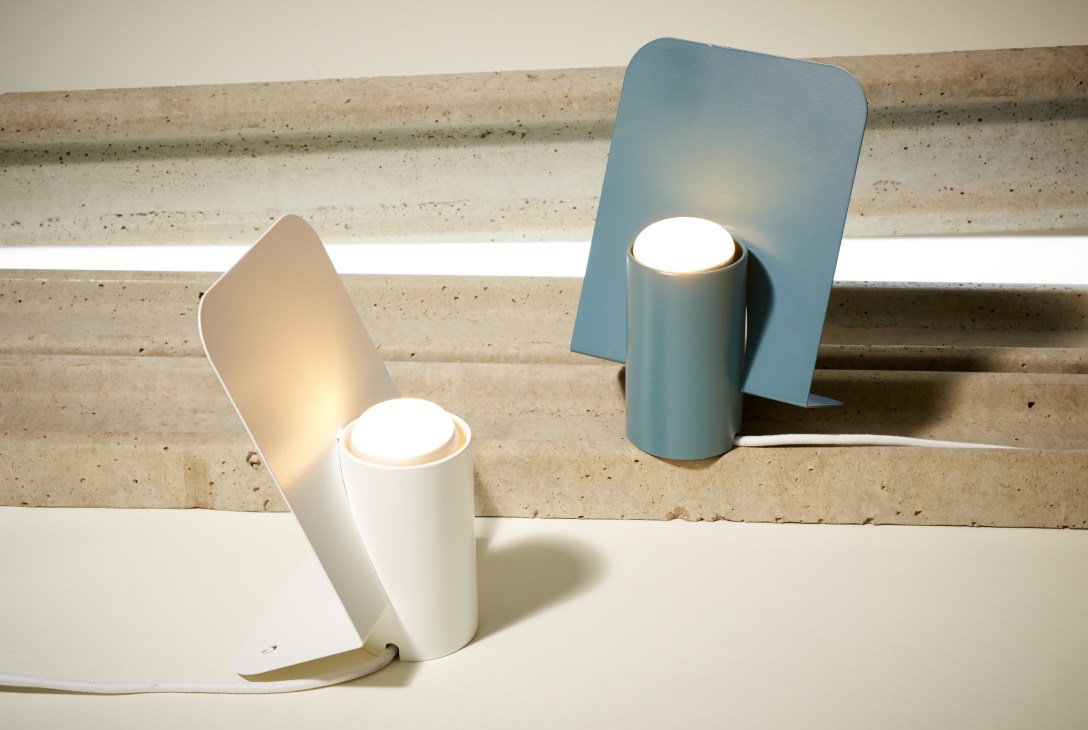 Two Vela lamps by Offiseria in white and blue with angular diffusers on concrete shelf.