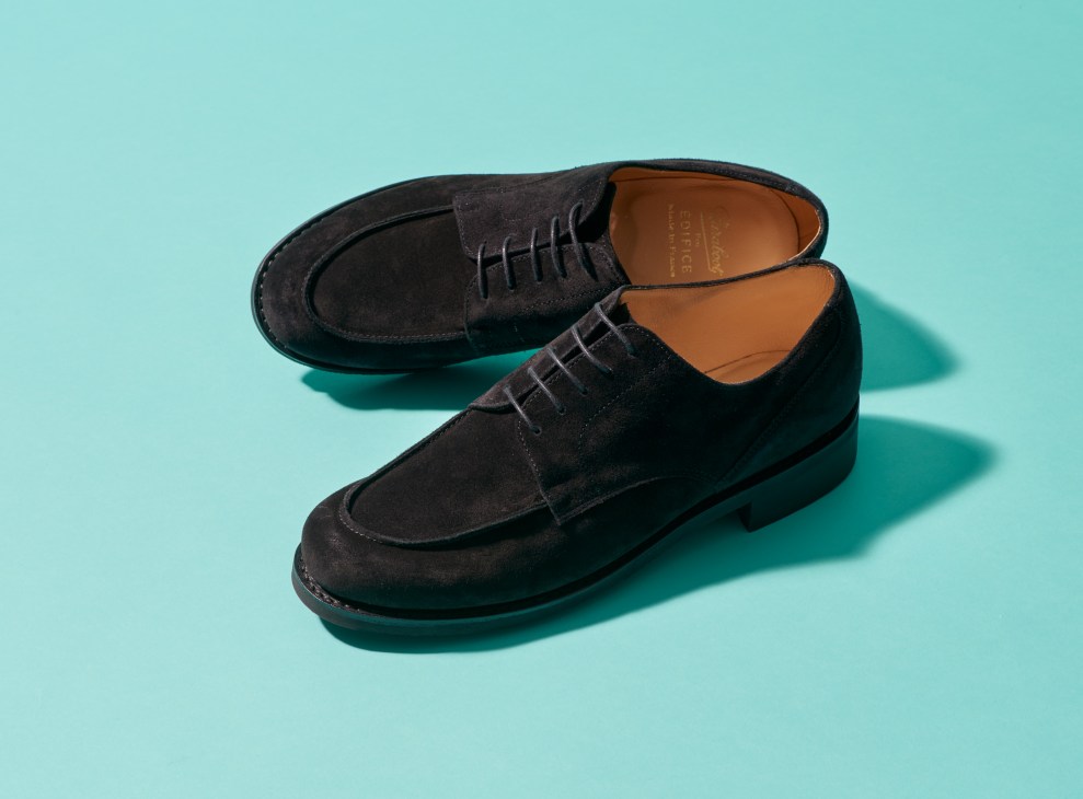 Pair of black suede lace-up shoes with tan leather insoles on a turquoise background.