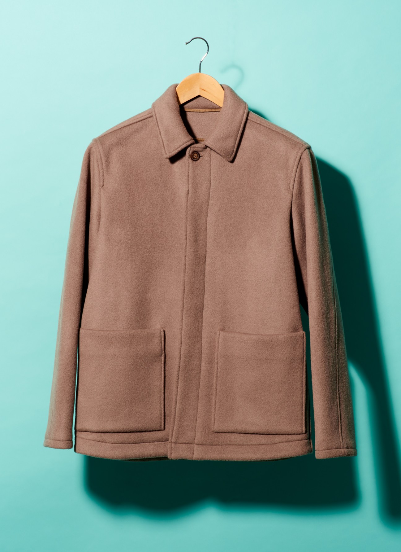 Taupe wool jacket on wooden hanger against turquoise background