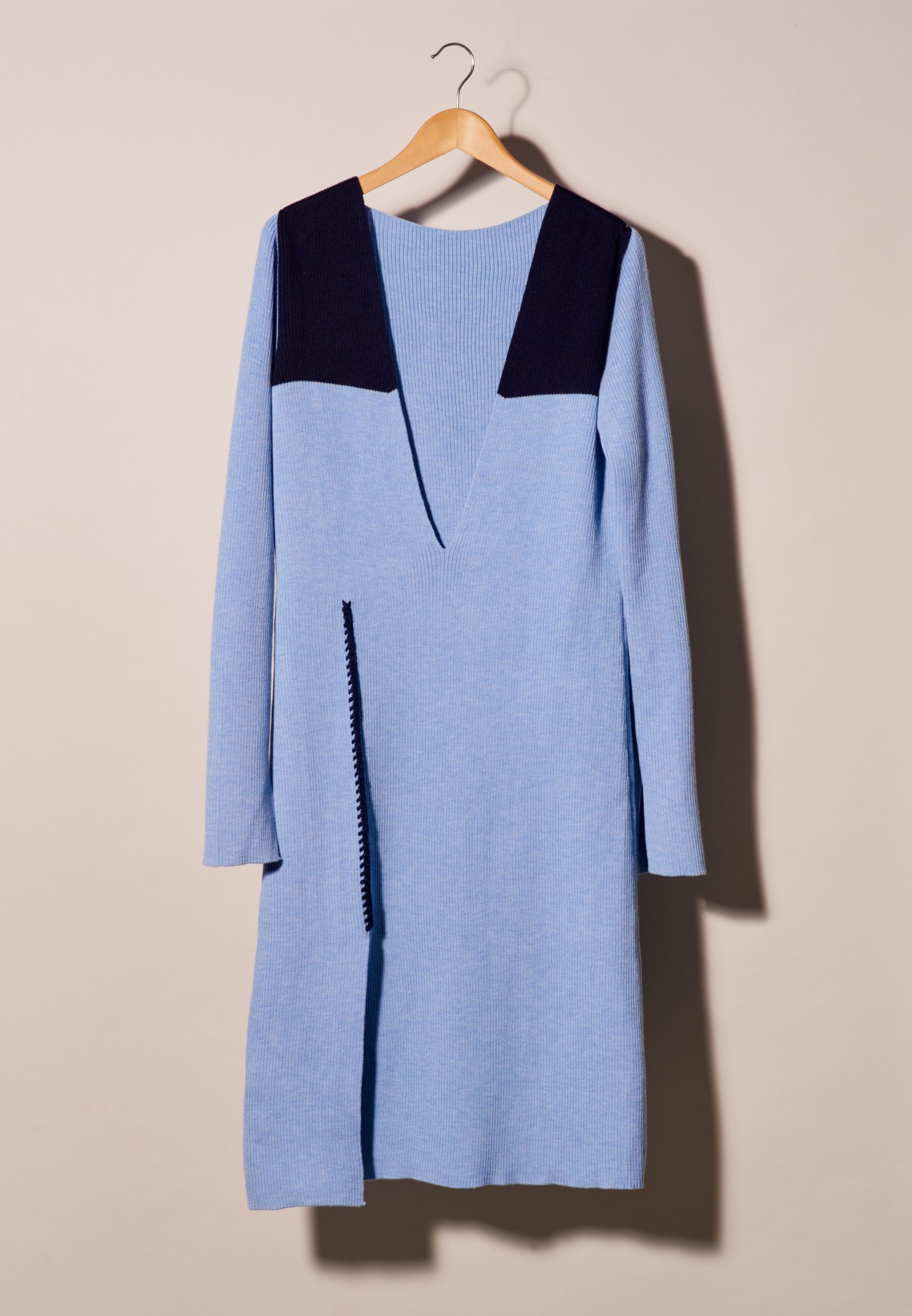 Light blue knit dress with navy colorblock detail on wooden hanger against beige background.