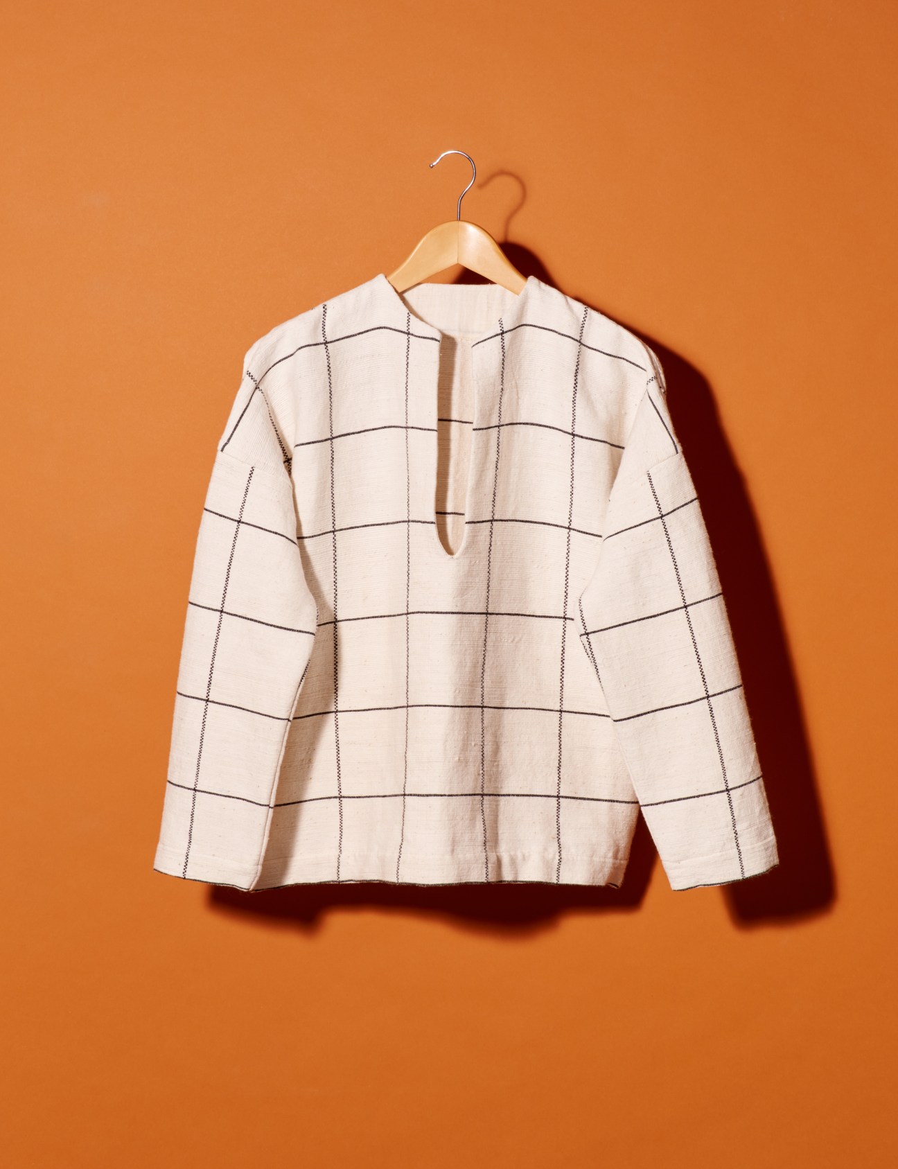 Cream-colored checked shirt on wooden hanger against orange background