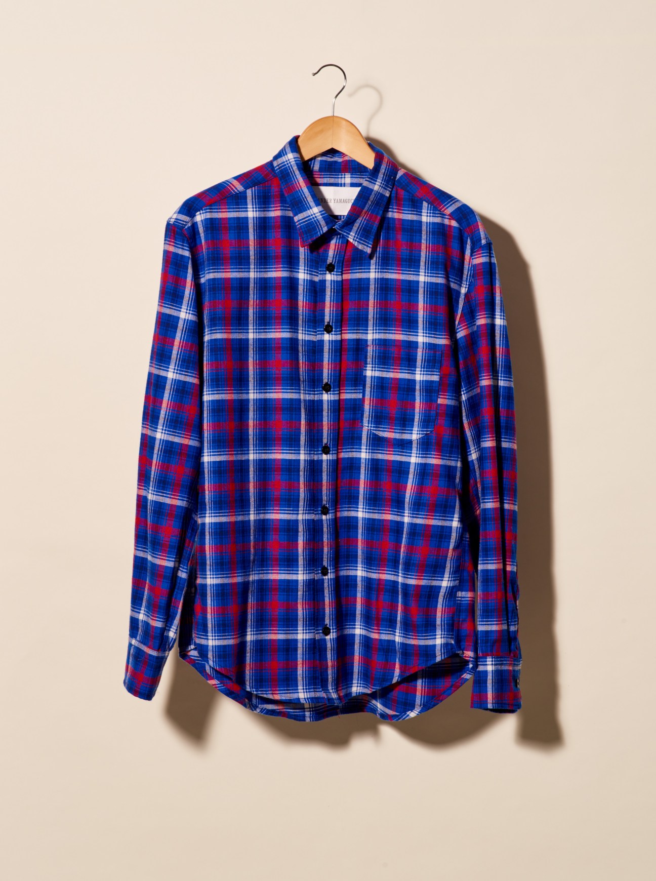 Blue, red and white checked button-up shirt by Alexander Yamaguchi on wooden hanger.