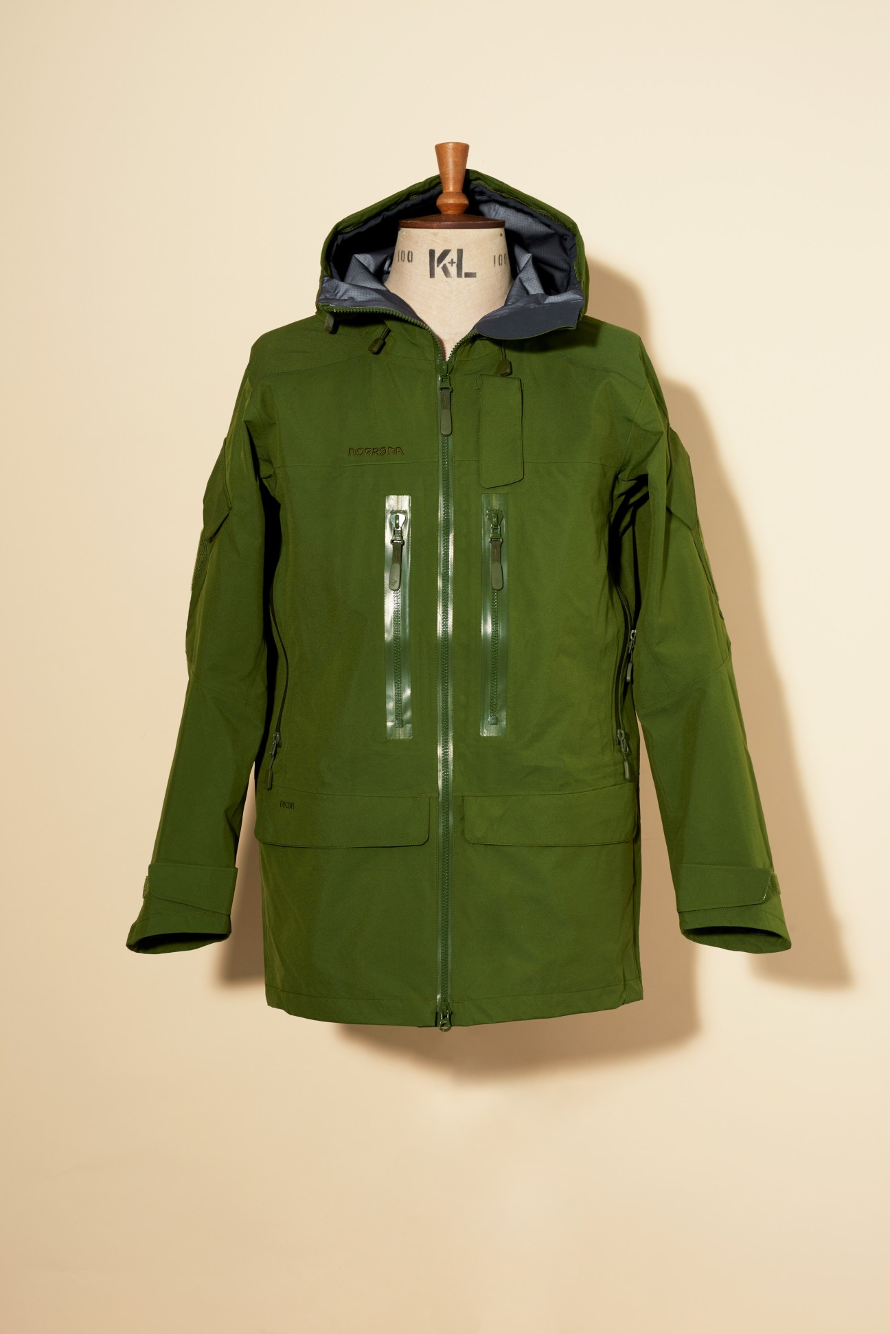 Norrona green Gore-Tex Pro jacket with hood displayed on a dress form against a beige background.