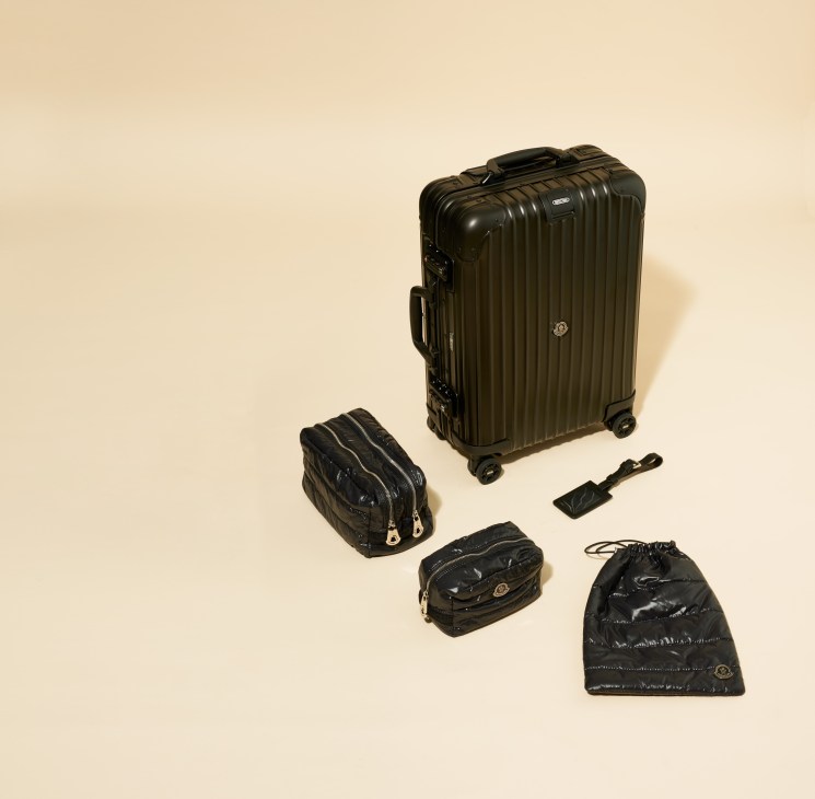 Rimowa x Moncler black cabin suitcase with matching puffy shoe bag, toiletry case and luggage tag on cream background.