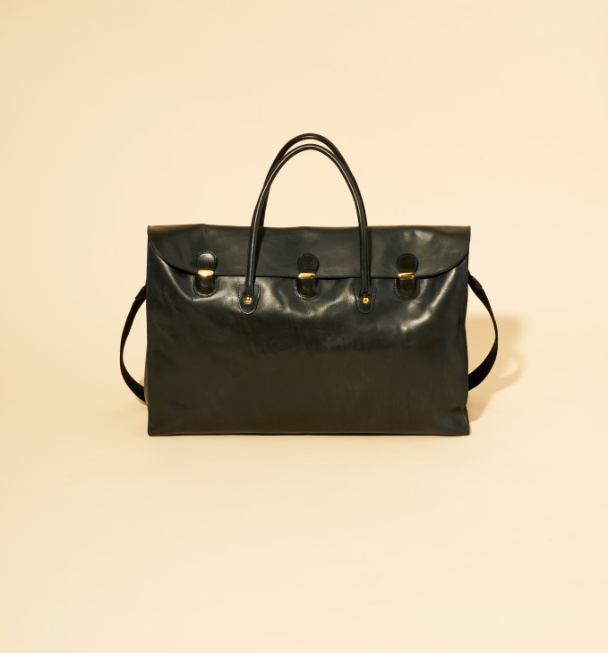 Black calf leather weekender bag by TL-180 with dual handles and gold hardware on cream background.