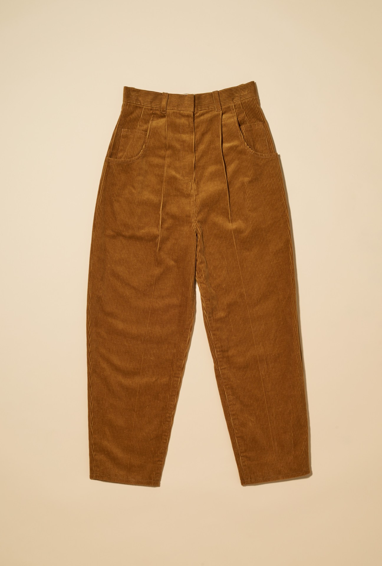 Tan corduroy trousers with high waist and straight legs on beige background.