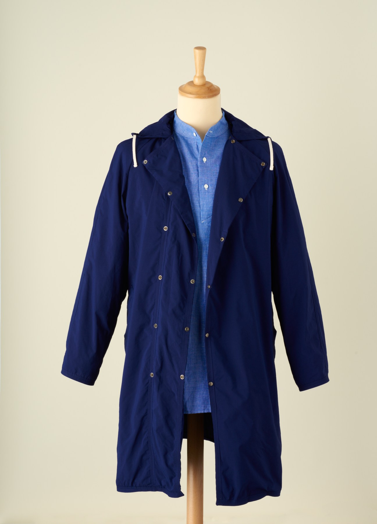 Navy blue jacket with blue shirt on wooden mannequin against beige background.