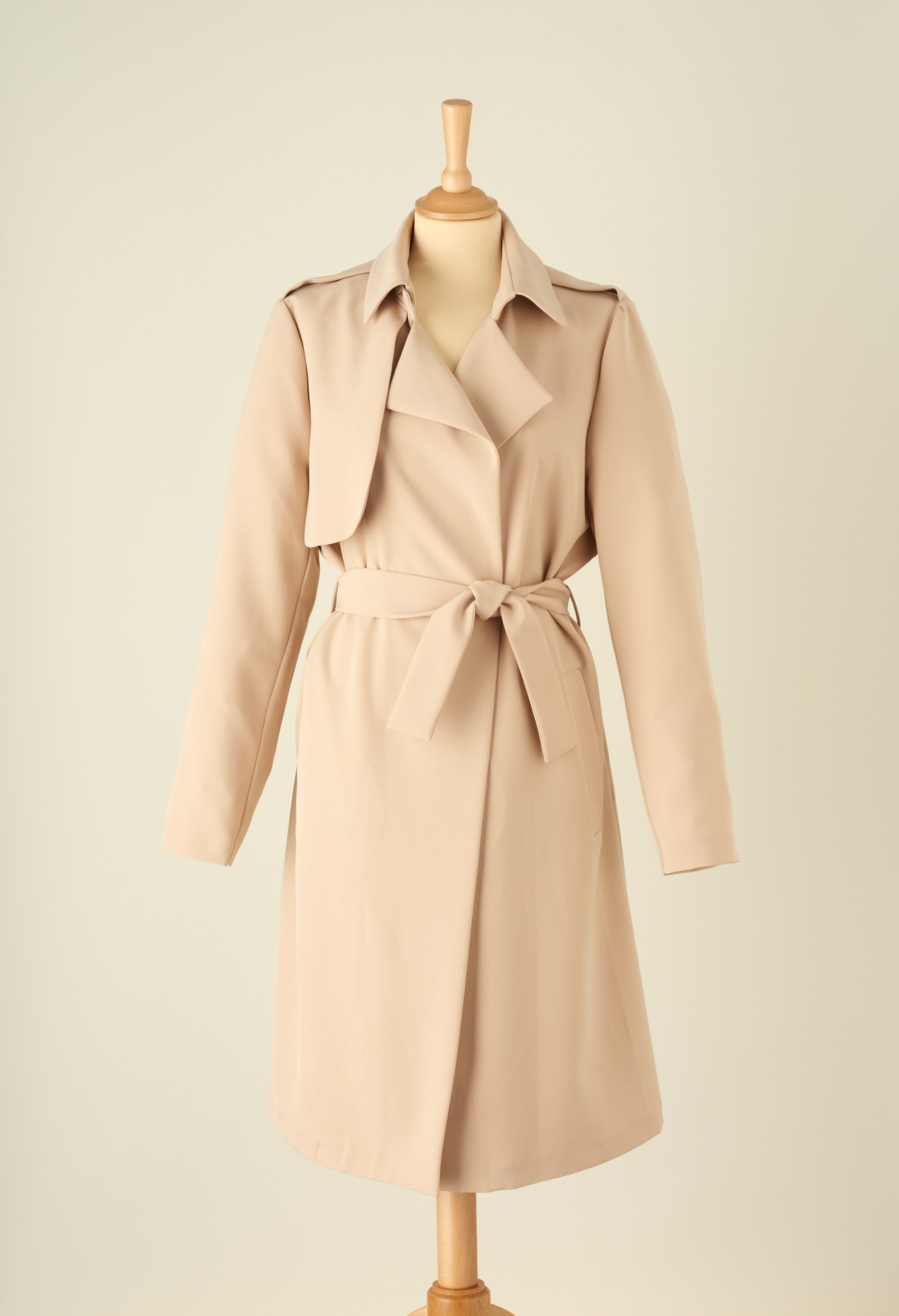 Beige trench coat with tailored silhouette displayed on dress form.
