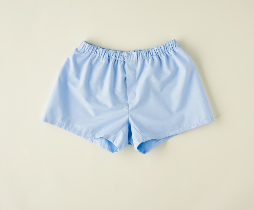 Light blue cotton boxer shorts with elastic waistband on beige background.