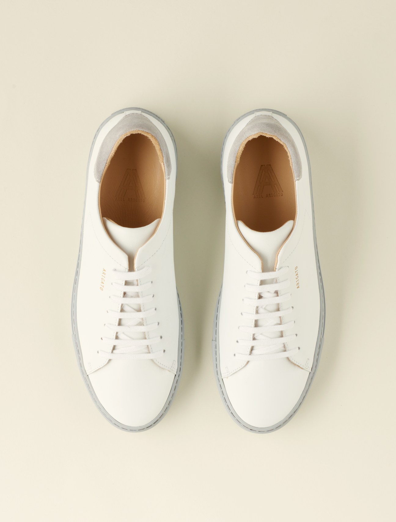 Pair of white leather high-top trainers with laces, shown from above on a neutral beige background.