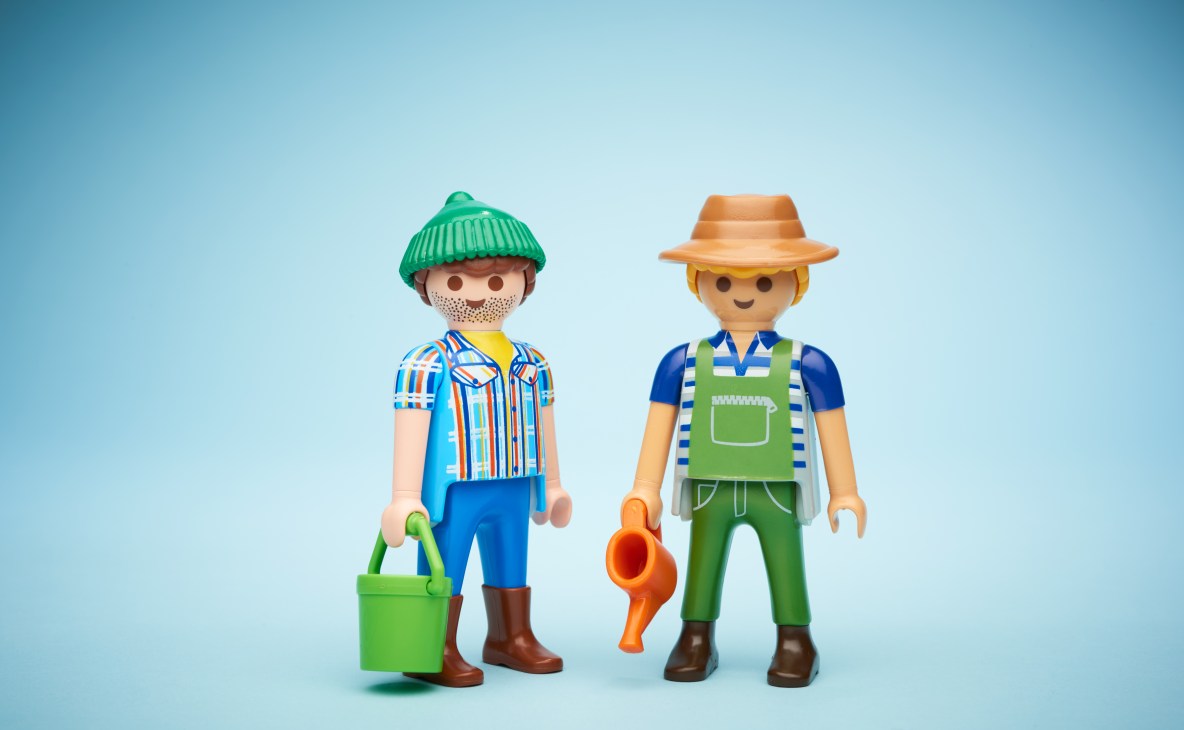 Two Playmobil figures dressed as workers with gardening tools against a blue background.