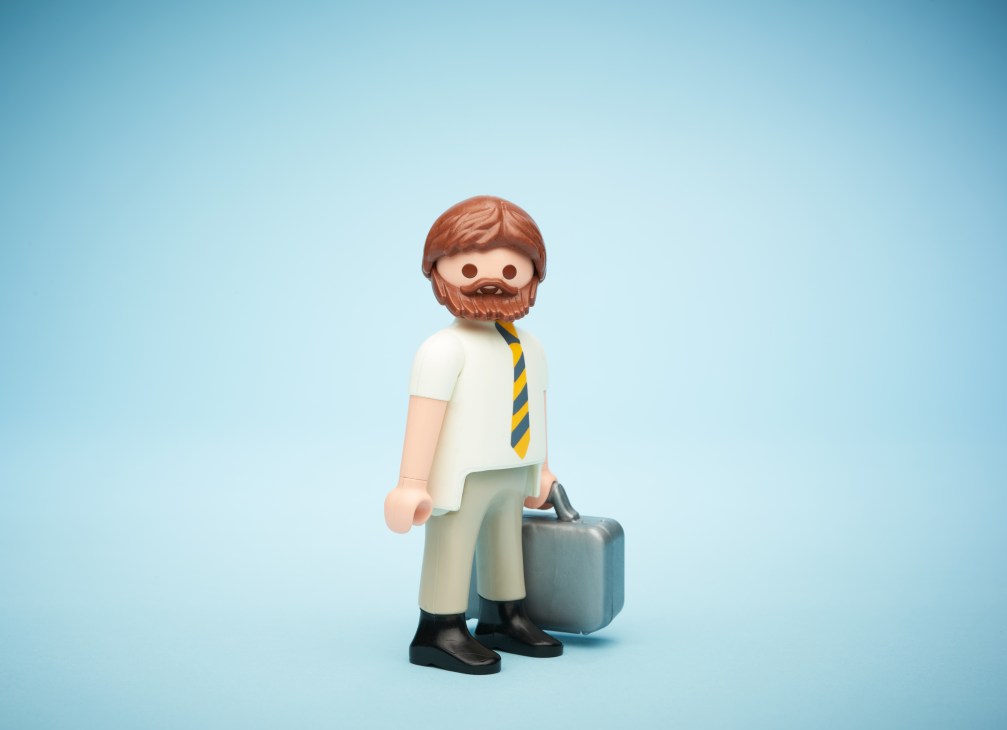 Playmobil figure of a bearded man in business attire holding a briefcase against a blue background.