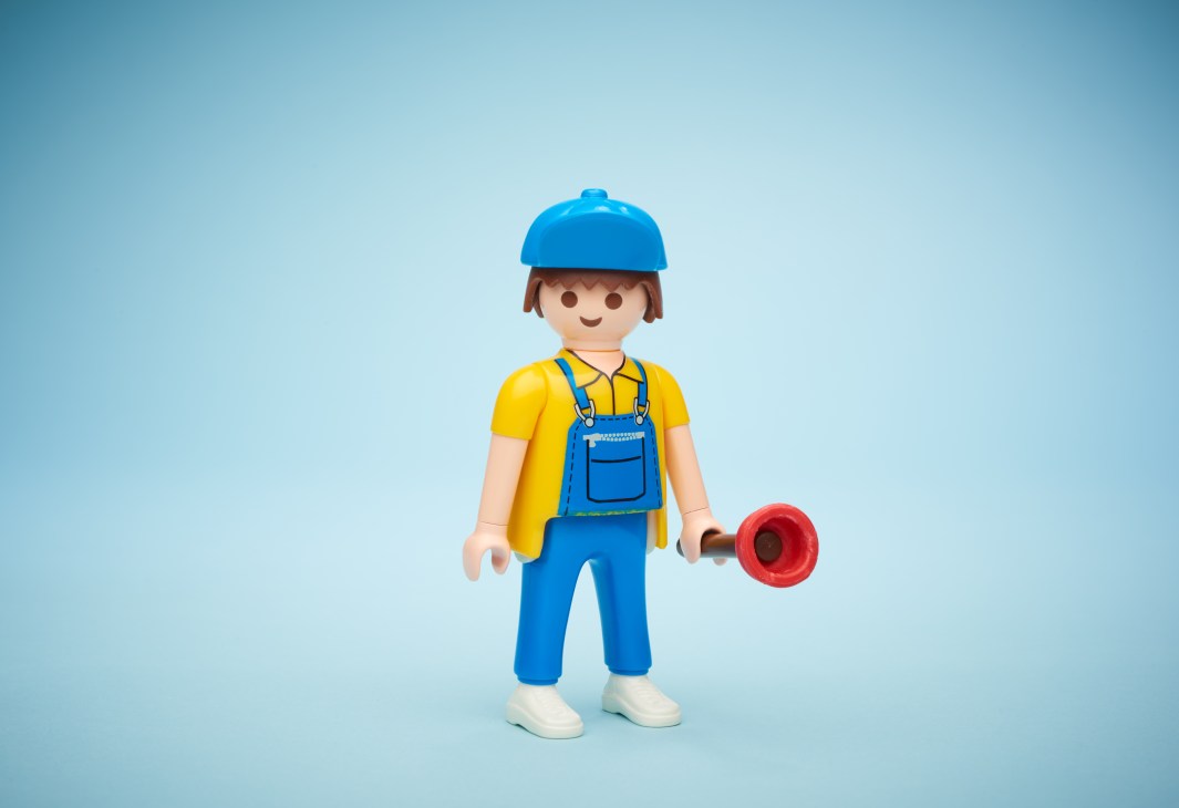 Playmobil figure of a handyman in blue overalls and cap holding a wrench against a light blue background.