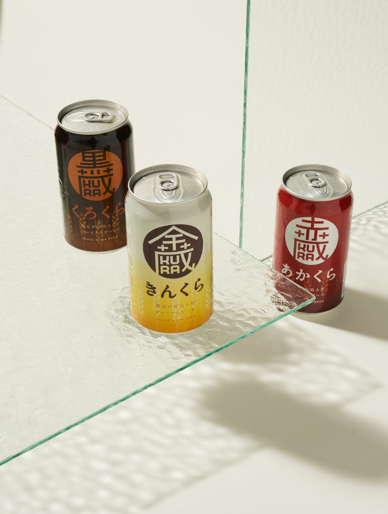 Three cans of Iwatekura craft beer with Japanese kanji characters on labels in dark, light yellow, and red.