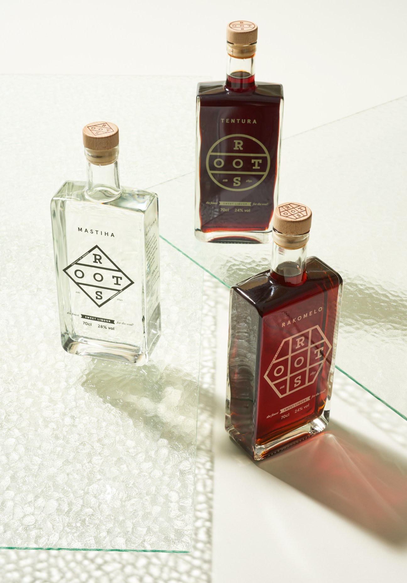 Three bottles of Finest Roots spirits with wooden cork stoppers and geometric diamond logo labels on white surface.